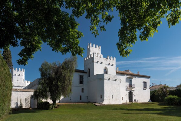 A white building with a tower and a large tree in the foreground. - Hospedium Hotel Cortijo Torre De La Reina (Guillena)