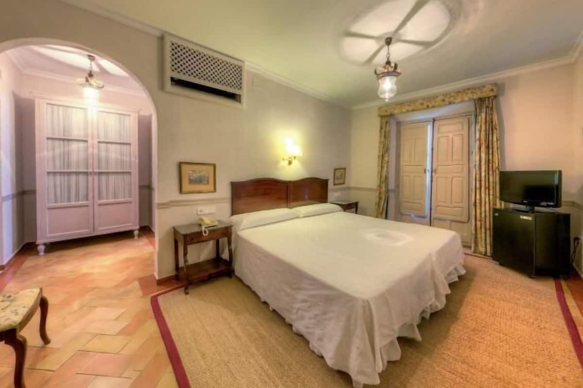Une chambre d’hôtel comprenant un lit, une table de chevet, une lampe, une armoire et un téléviseur.