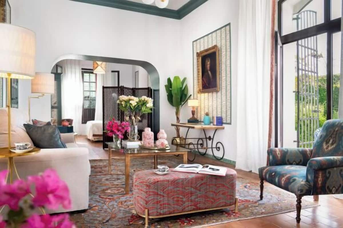 Un salon bien éclairé, comprenant un canapé, un fauteuil, un pouf et une table basse agrémentée d’objets décoratifs.