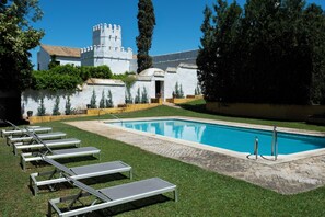 A swimming pool with lounge chairs and a castle-like building in the background. - Hospedium Hotel Cortijo Torre De La Reina (Guillena)