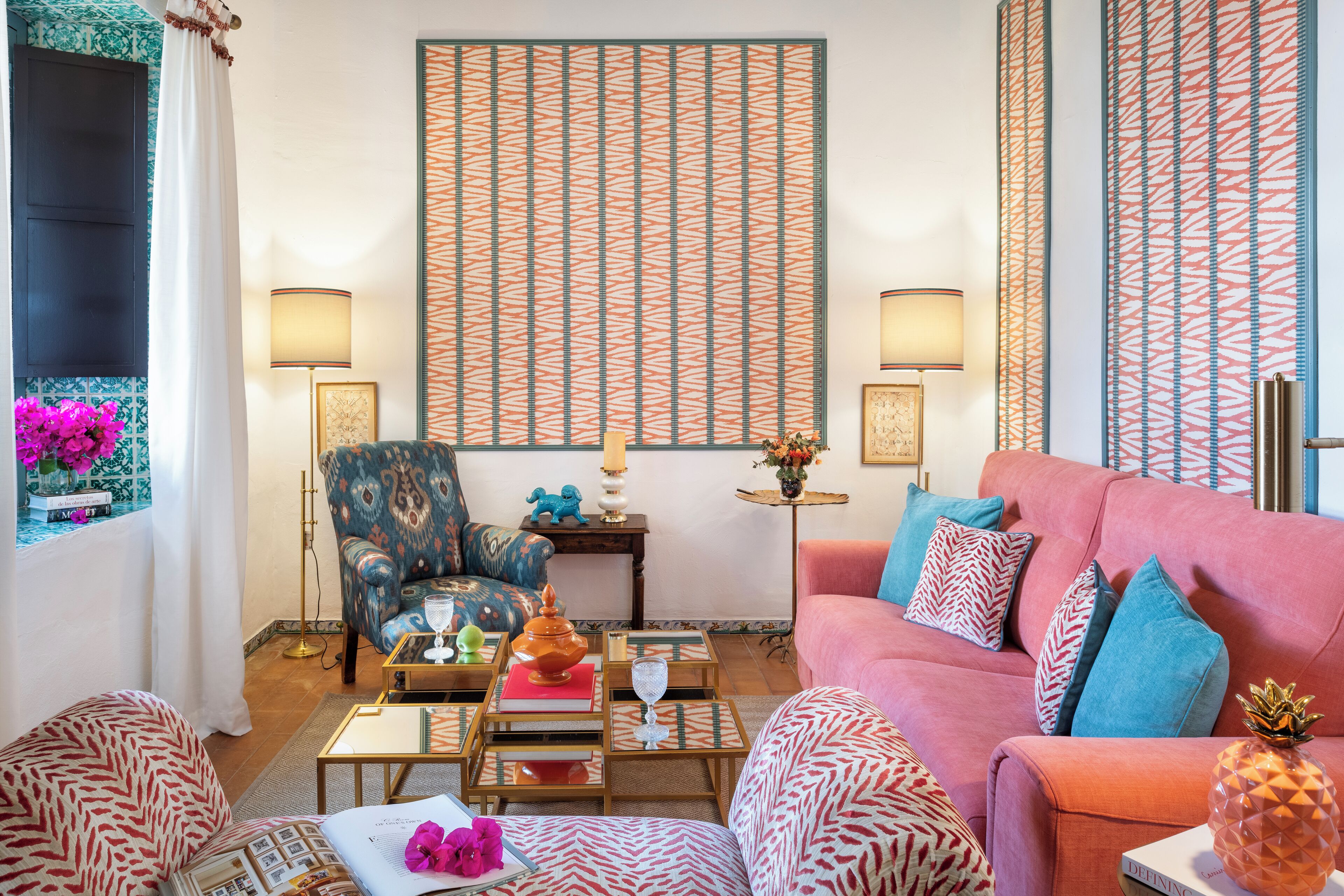 Ein Wohnzimmer mit gemustertem Wandpapier, einer Couch, Sesseln und einem Couchtisch mit Dekoration.
