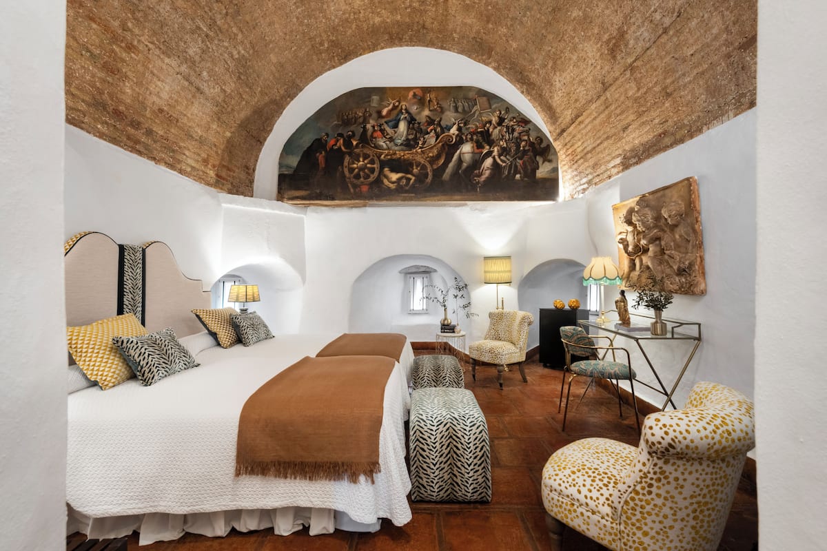 Une chambre spacieuse avec un grand lit, une chaise, un bureau et une fresque murale.