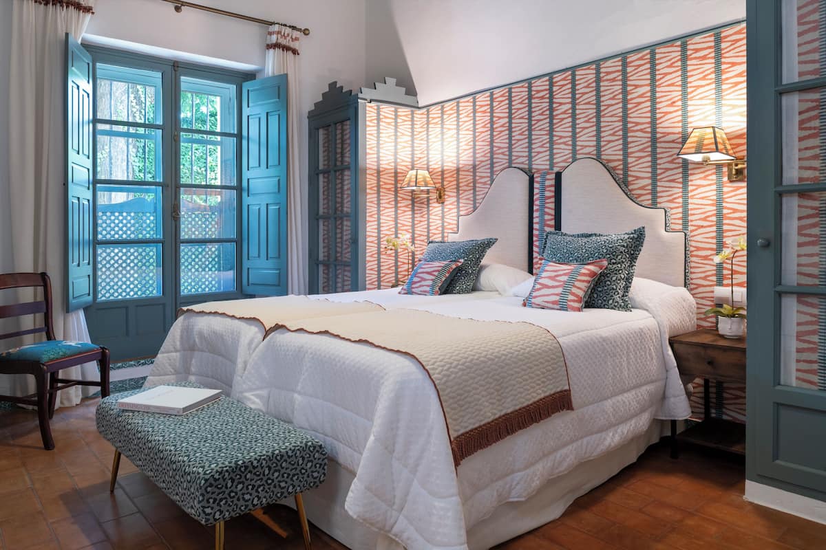 Une chambre à coucher avec un grand lit, une chaise, une table de chevet et une fenêtre avec des rideaux.