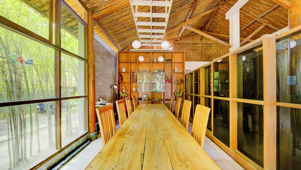 A long wooden table with chairs, large windows, and a ceiling with wooden beams and a hanging light fixture. - Capital O 3840 Java Hotel & Resto (Cilacap)