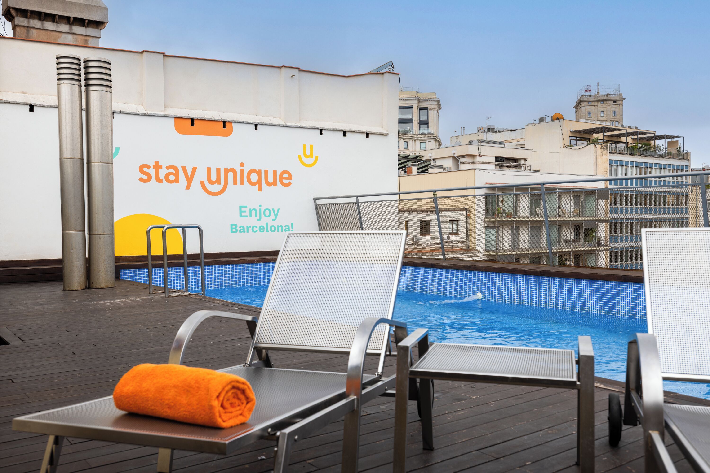 Un área de piscina en la azotea con sillas de descanso, una toalla y un cartel que dice 'stay unique'.