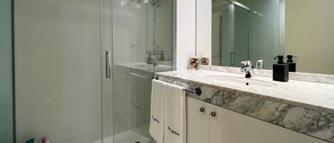 A modern bathroom with a glass-enclosed shower, a marble sink, and a large mirror.