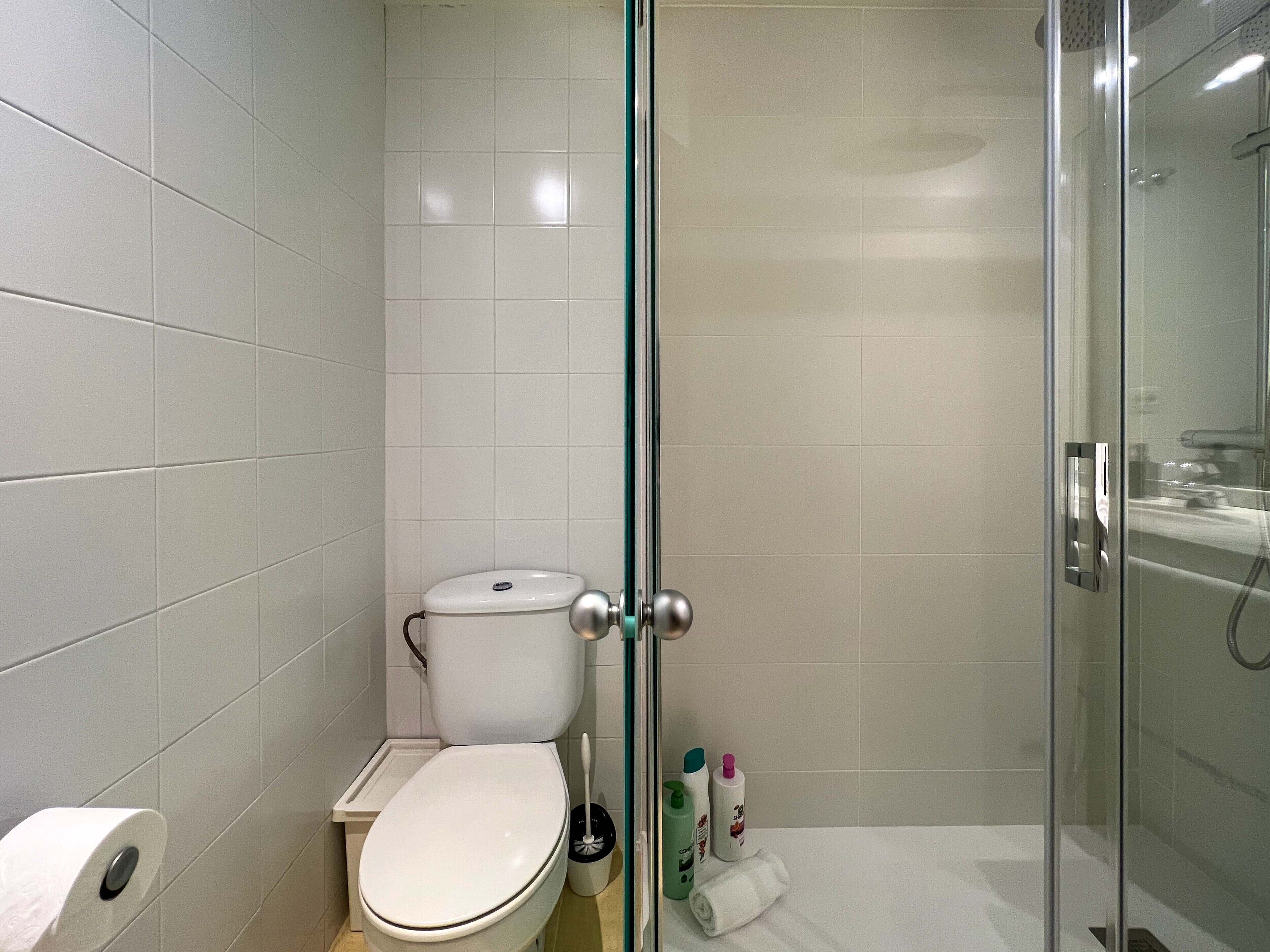 A bathroom with a toilet, a glass shower enclosure, and a towel on the floor.