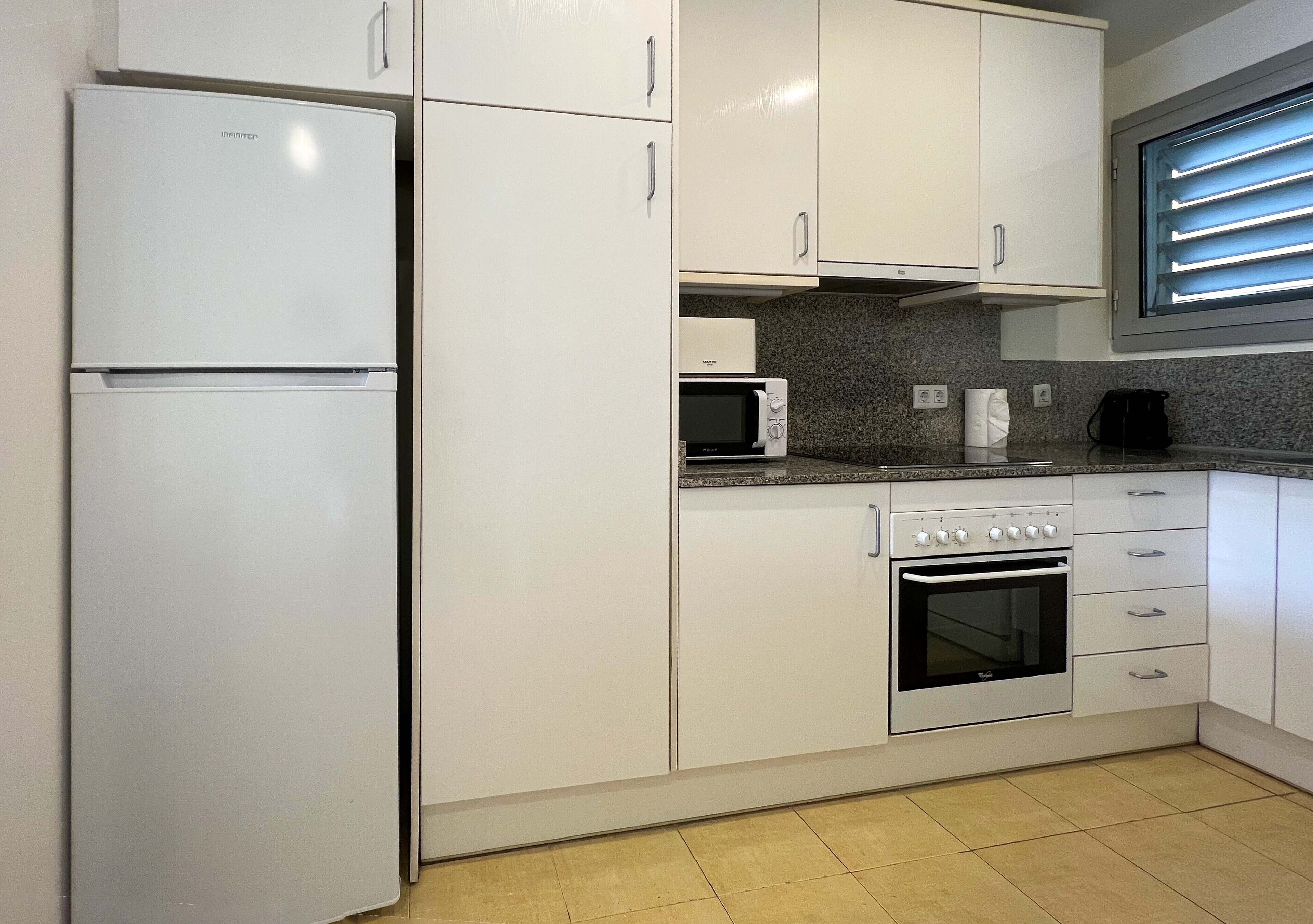 A kitchen with white cabinets, a built-in microwave, a stove, and a refrigerator.