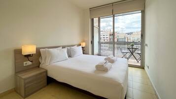 Una habitación de hotel con una cama grande, dos lámparas de noche, una mesita de noche y un balcón con vistas a la ciudad.