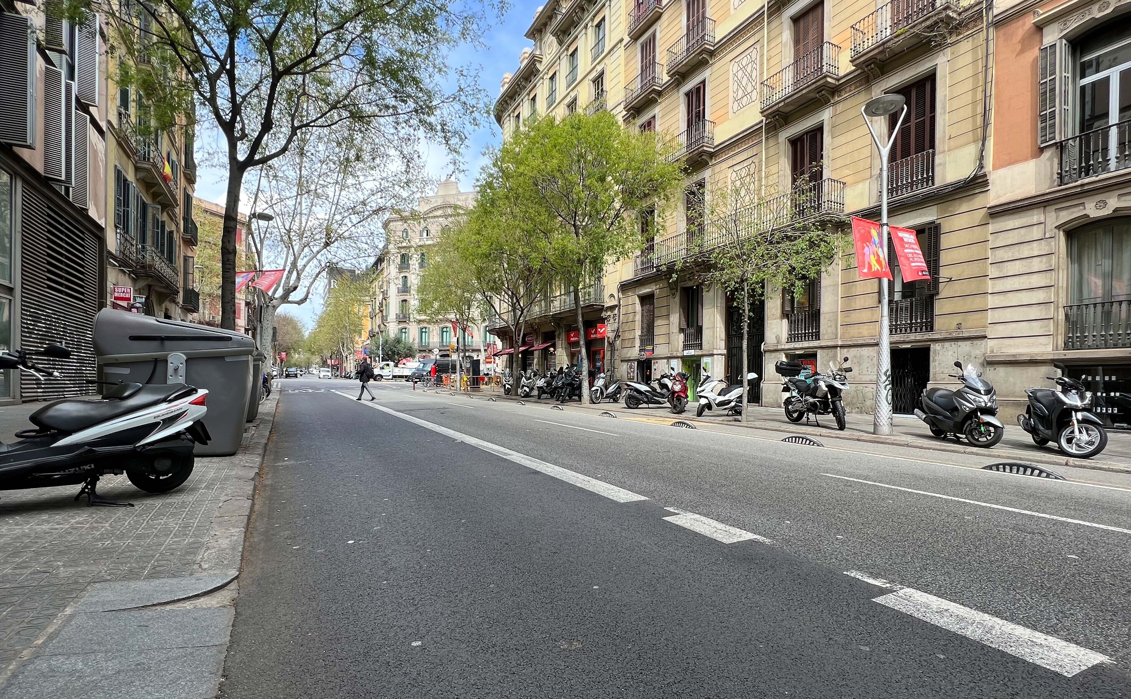 Een straat met geparkeerde scooters en motorfietsen, gebouwen met balkons en bomen.