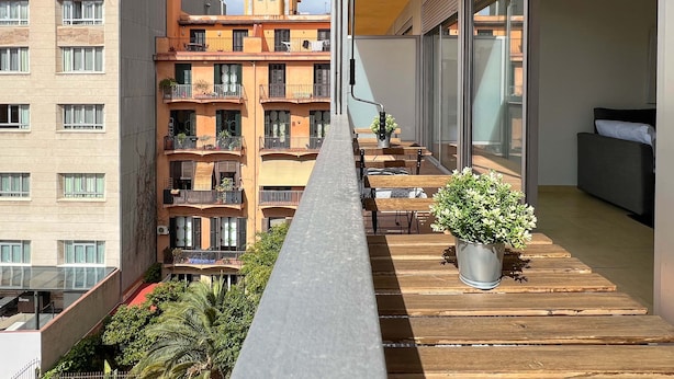Een balkon met houten vloer, een plant in pot en uitzicht op omliggende gebouwen.