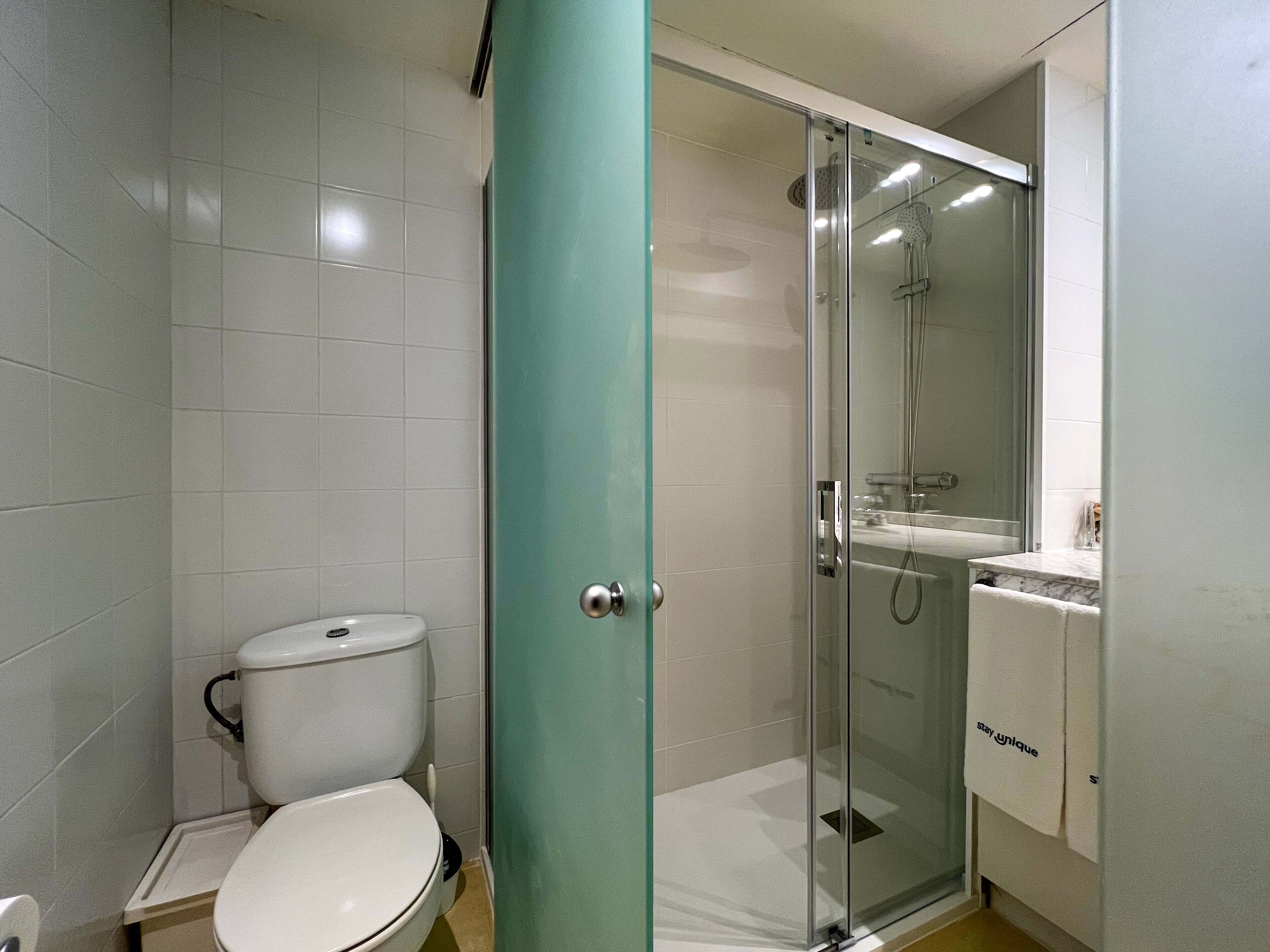 A bathroom with a toilet, a glass shower enclosure, and a sink with a towel hanging on the wall.