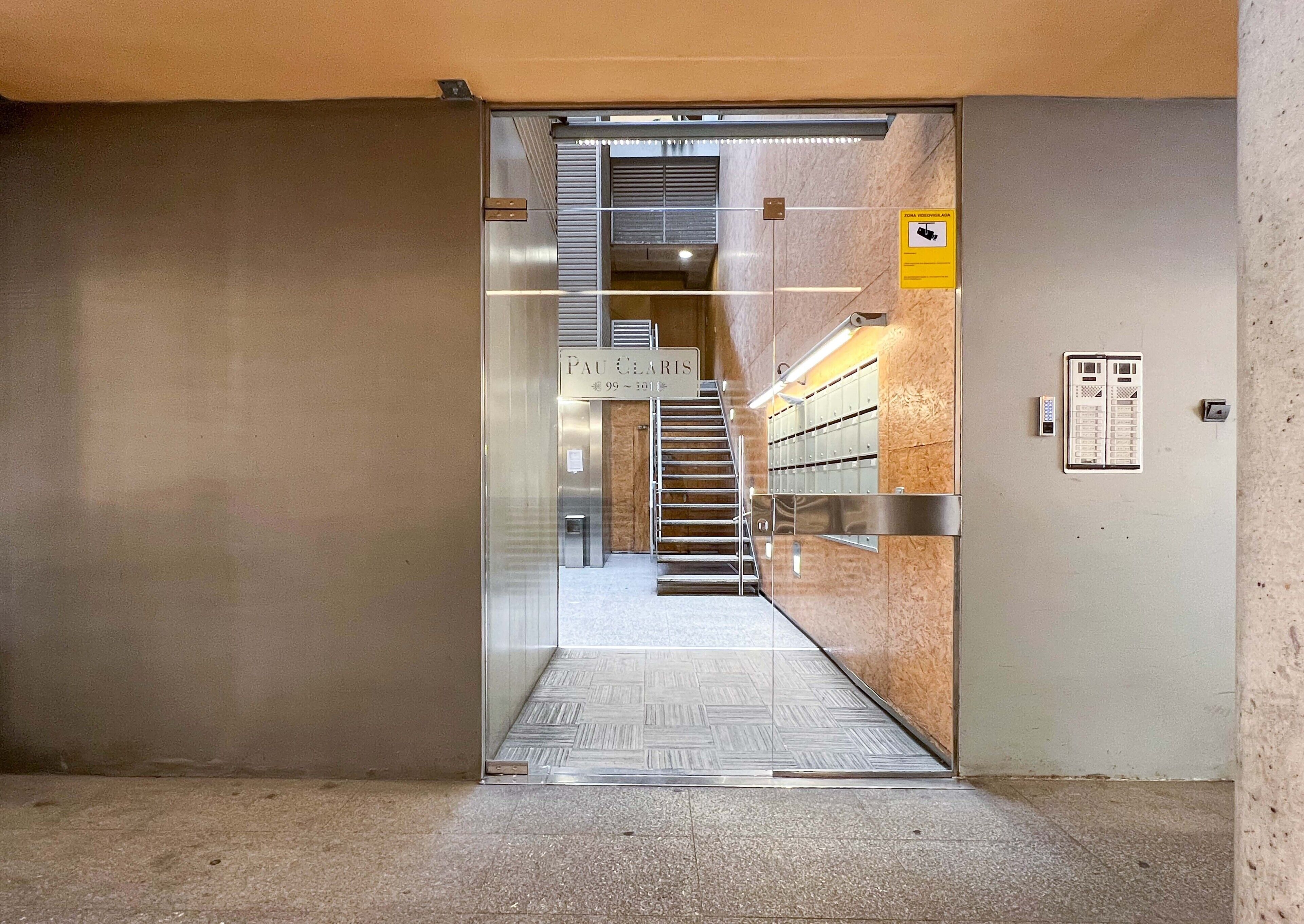 Entrada de ascensor con un cartel que indica "Pau C'harris" y una escalera que sube a un piso superior.