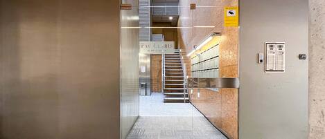 Entrada de ascensor con un cartel que indica "Pau C'harris" y una escalera que sube a un piso superior.