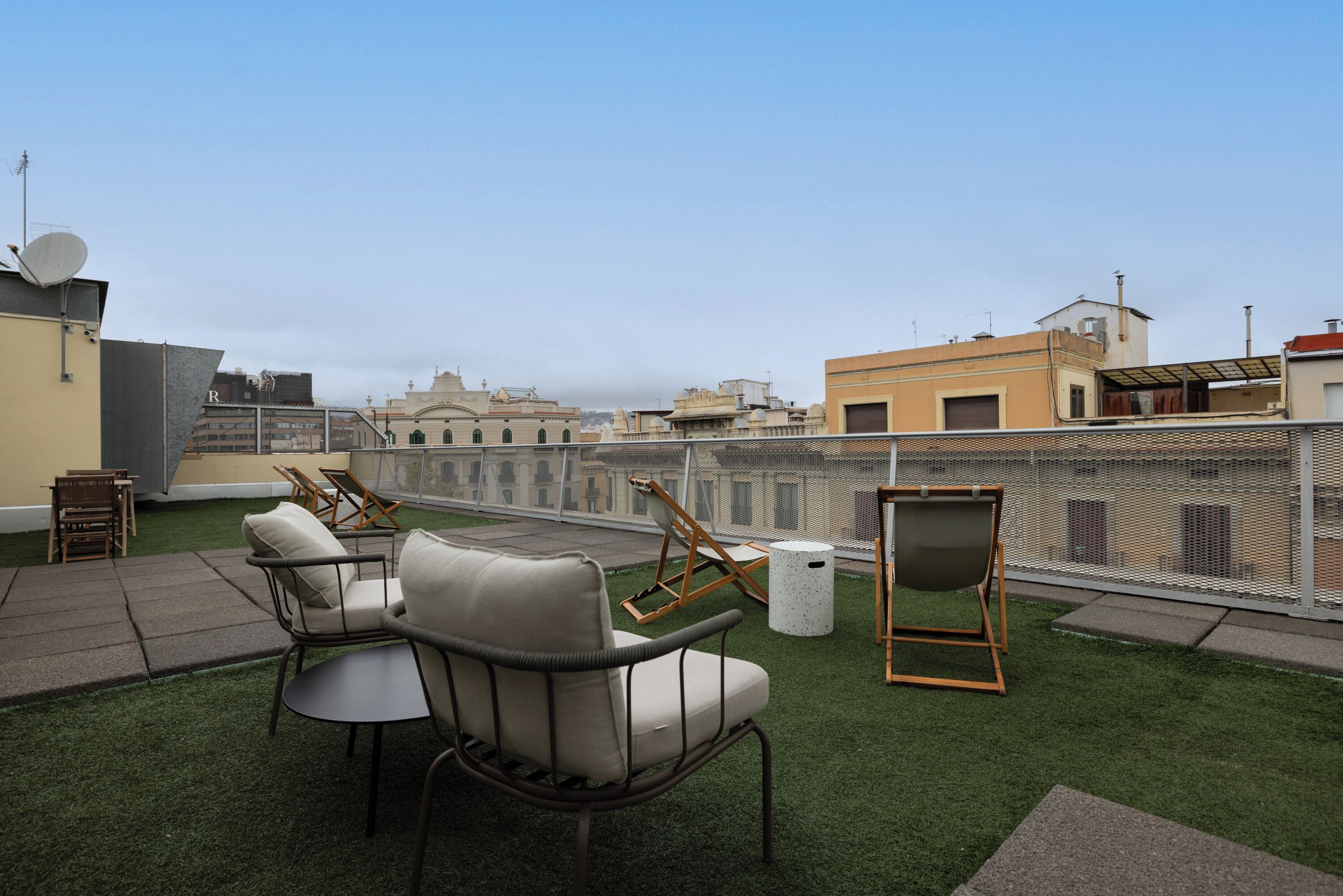 A rooftop terrace with outdoor furniture, a satellite dish, and a view of city buildings.