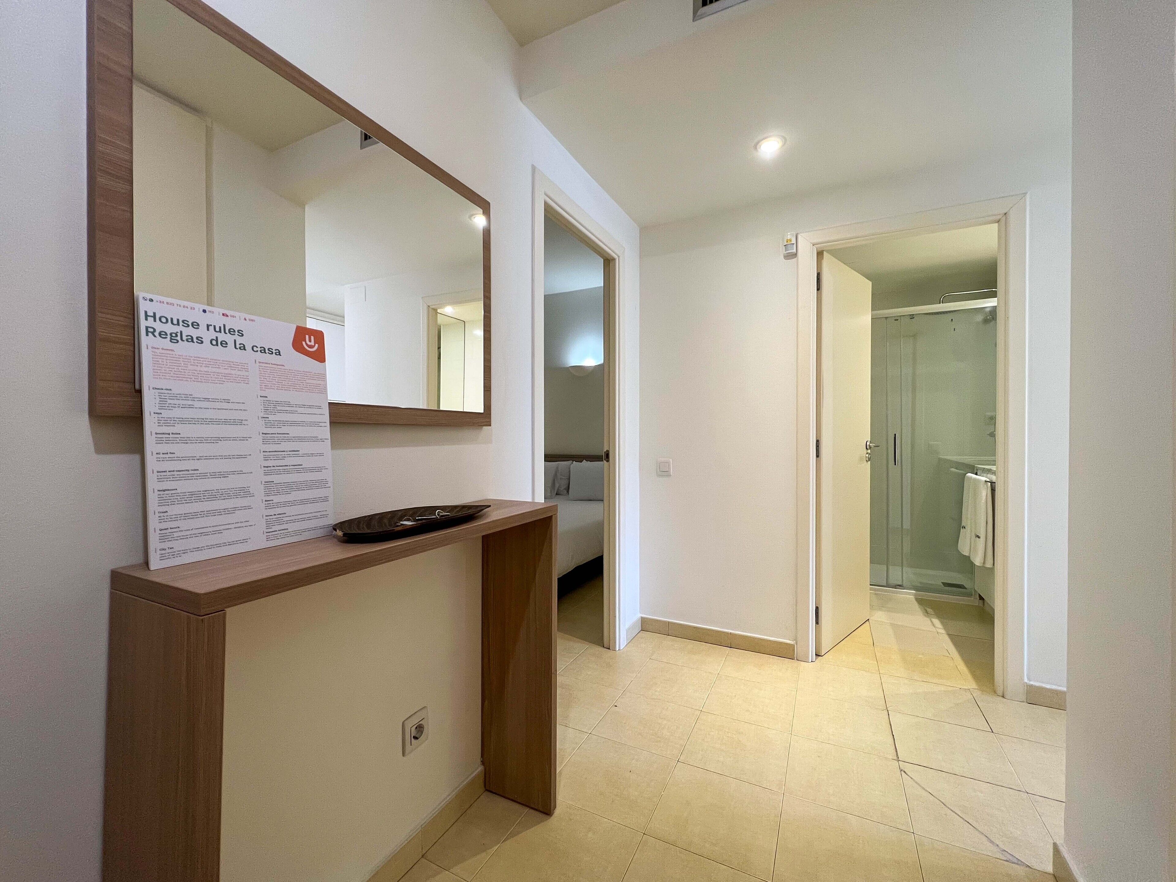 A hallway with a wooden reception desk, a large mirror, and a sign with house rules.