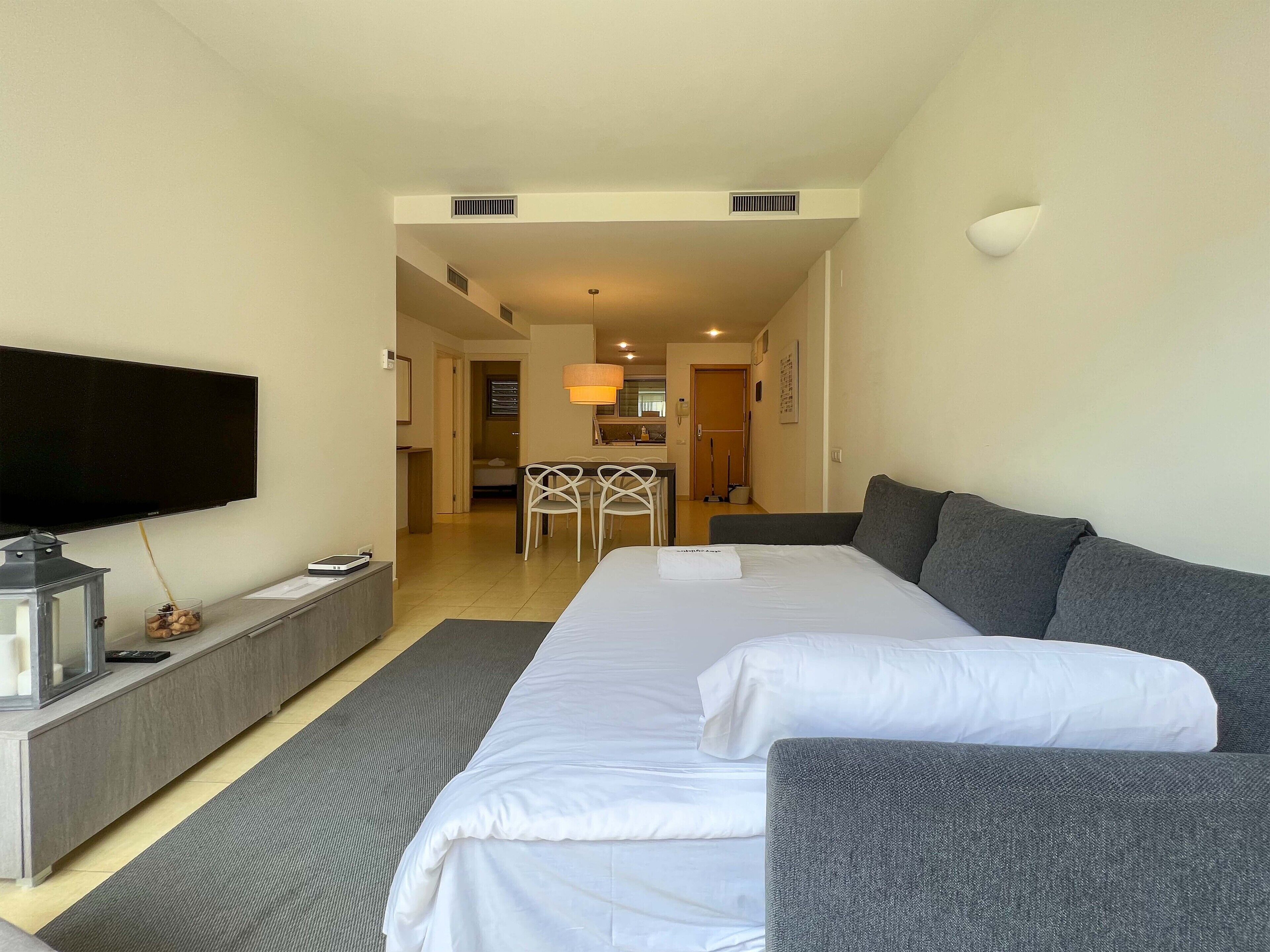 A hotel room with a large bed, a TV, a desk, and a dining area in the background.