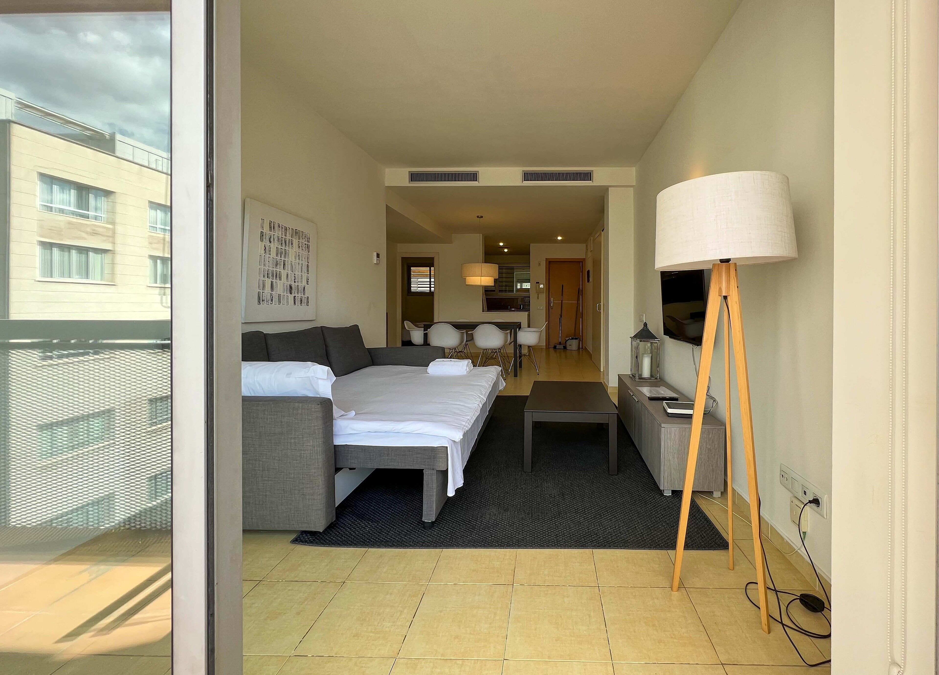 Habitació d'hotel moderna amb llit, sofà, escriptori, làmpada i vista de l'edifici exterior.