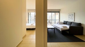Een moderne hotelkamer met een bed, een slaapbank, een eettafel en een balkon met uitzicht op de stad.