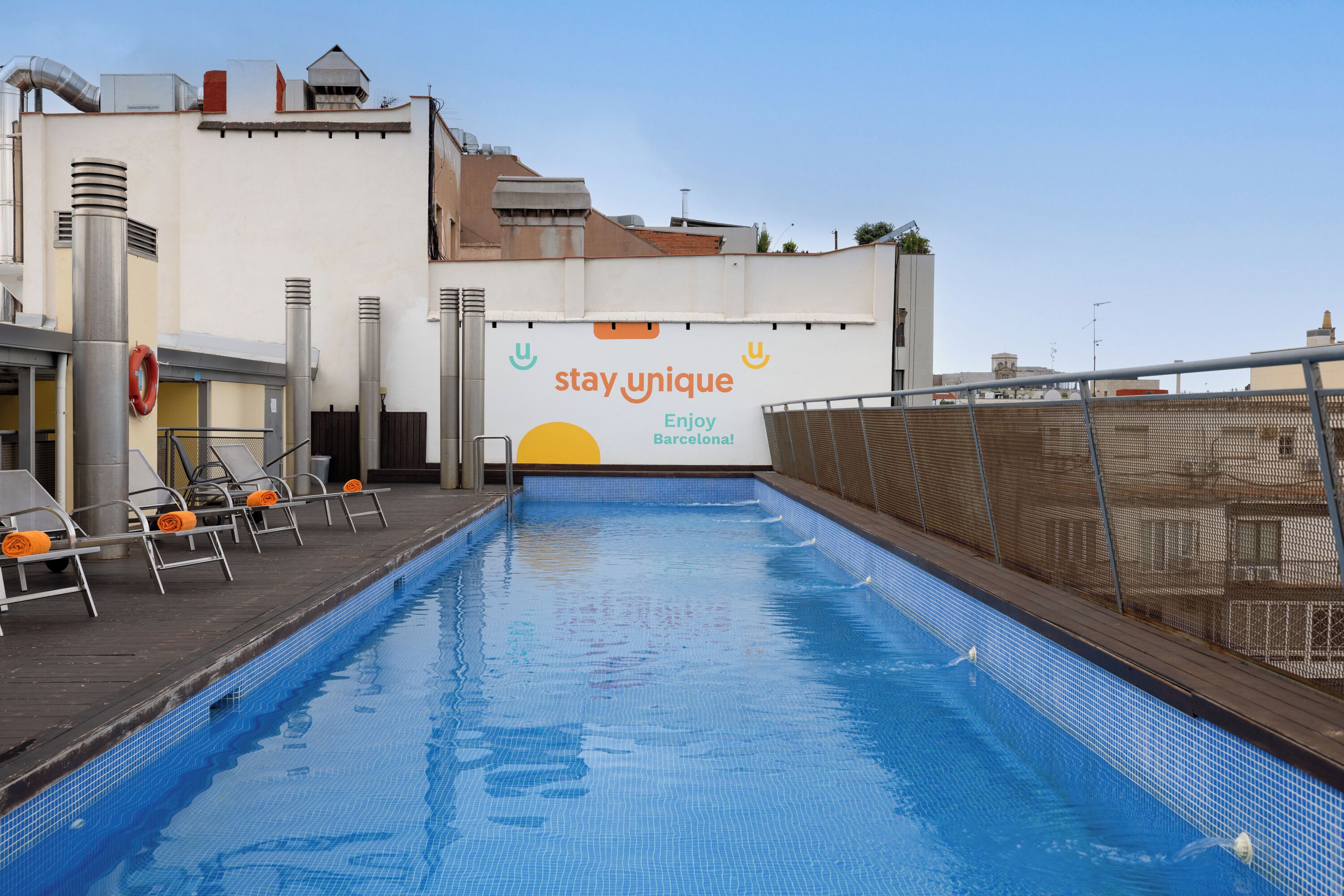 An indoor swimming pool with a 'stay unique' sign, lounge chairs, and a view of the cityscape.