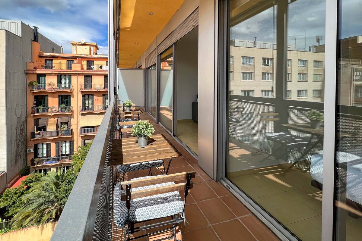 Ein Balkon mit einem Holztisch und Stühlen, Blumentöpfen und Blick auf benachbarte Gebäude.