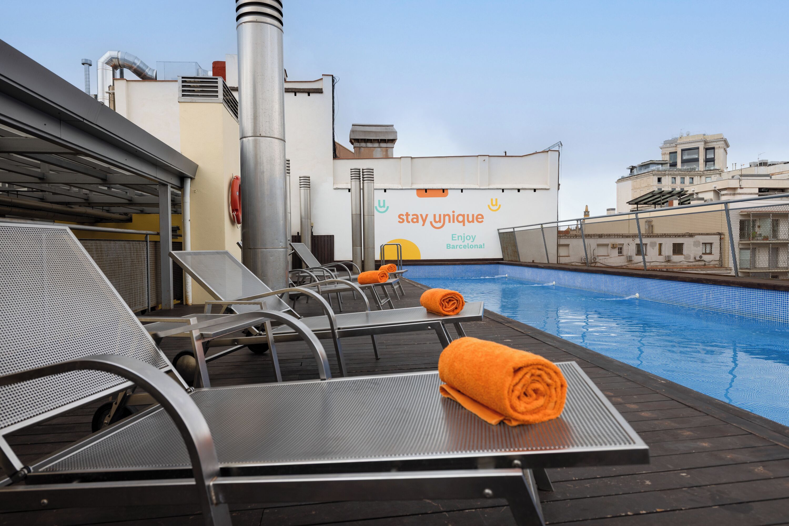 A rooftop pool area with lounge chairs, a towel, and a 'stay_unique' sign.