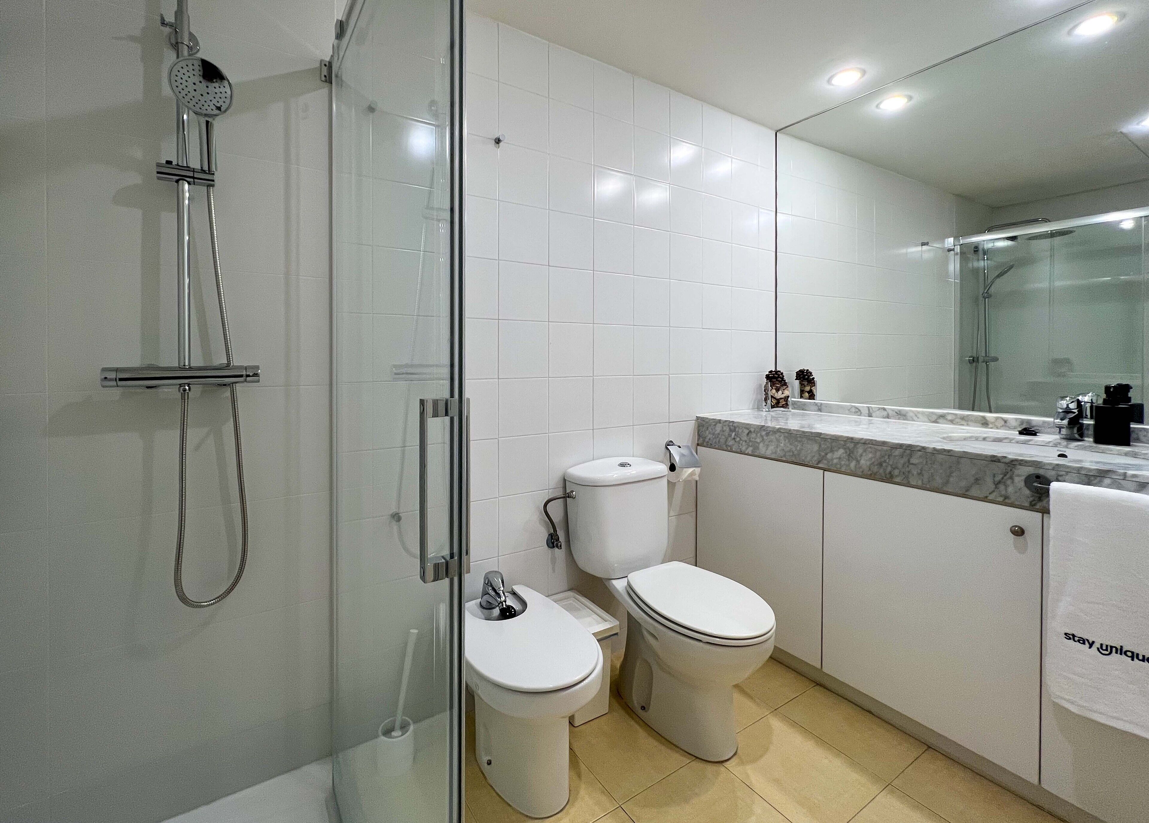 Uma casa de banho moderna com cabine de duche em vidro, sanita e lavatório com bancada em mármore.