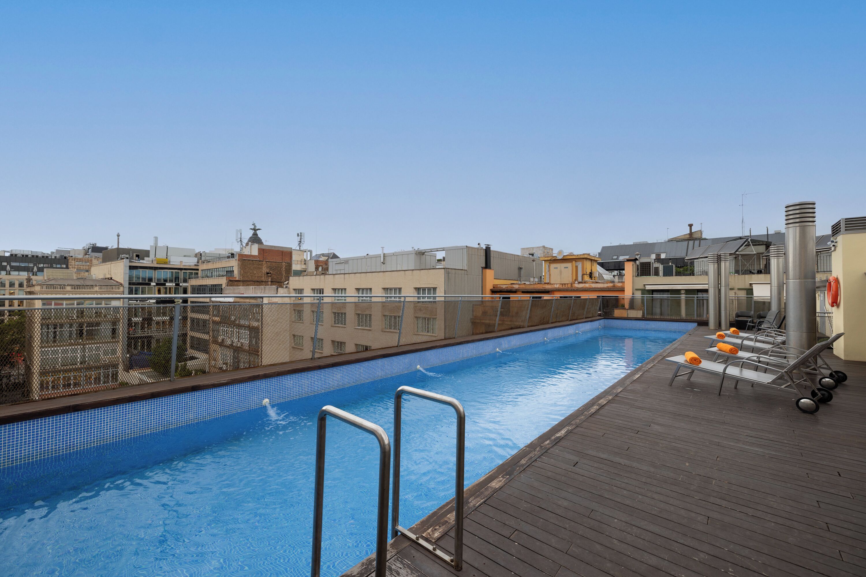 A rooftop swimming pool with a wooden deck, metal railings, and lounge chairs.