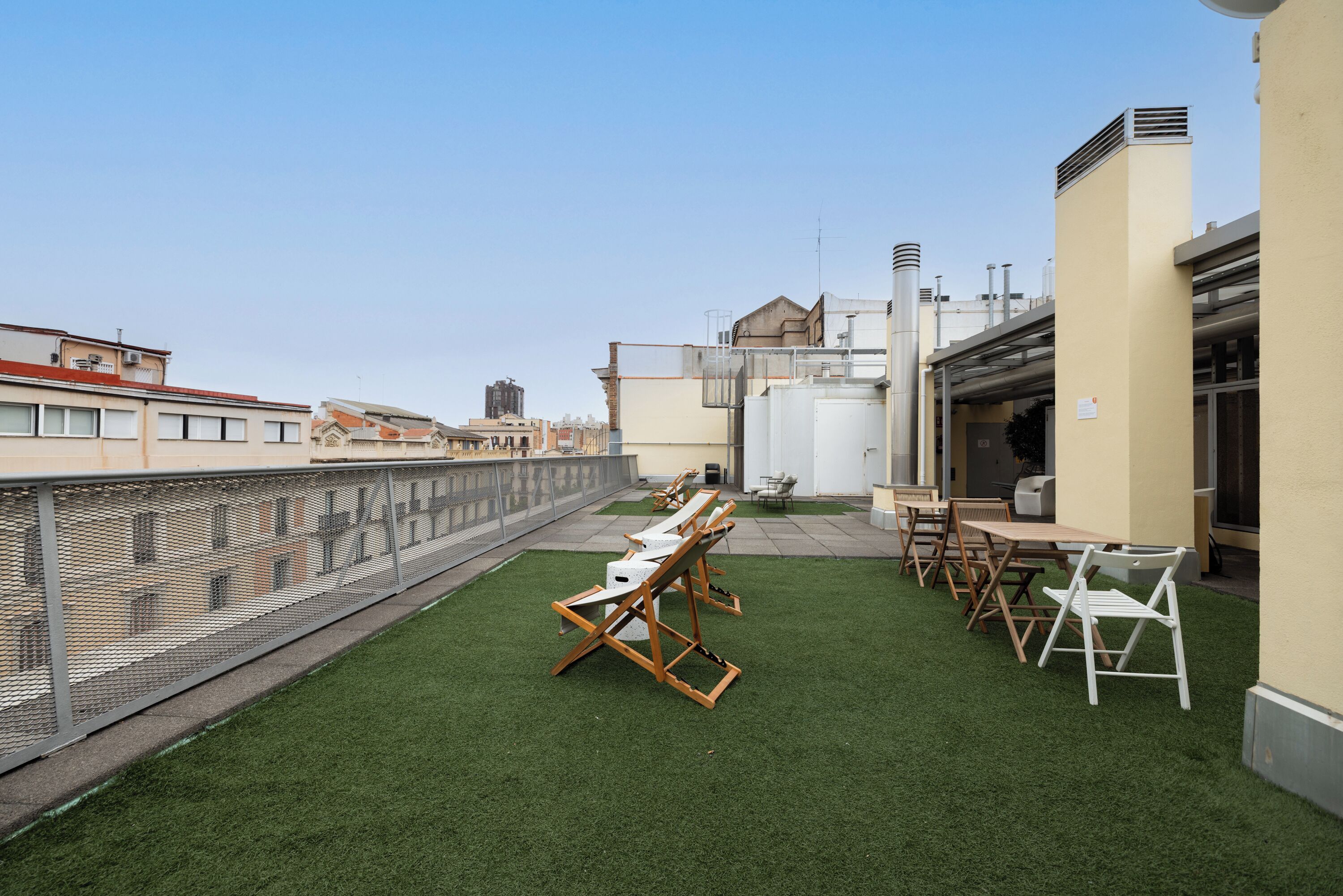 A rooftop terrace with artificial grass, outdoor seating, and industrial-style buildings in the background.