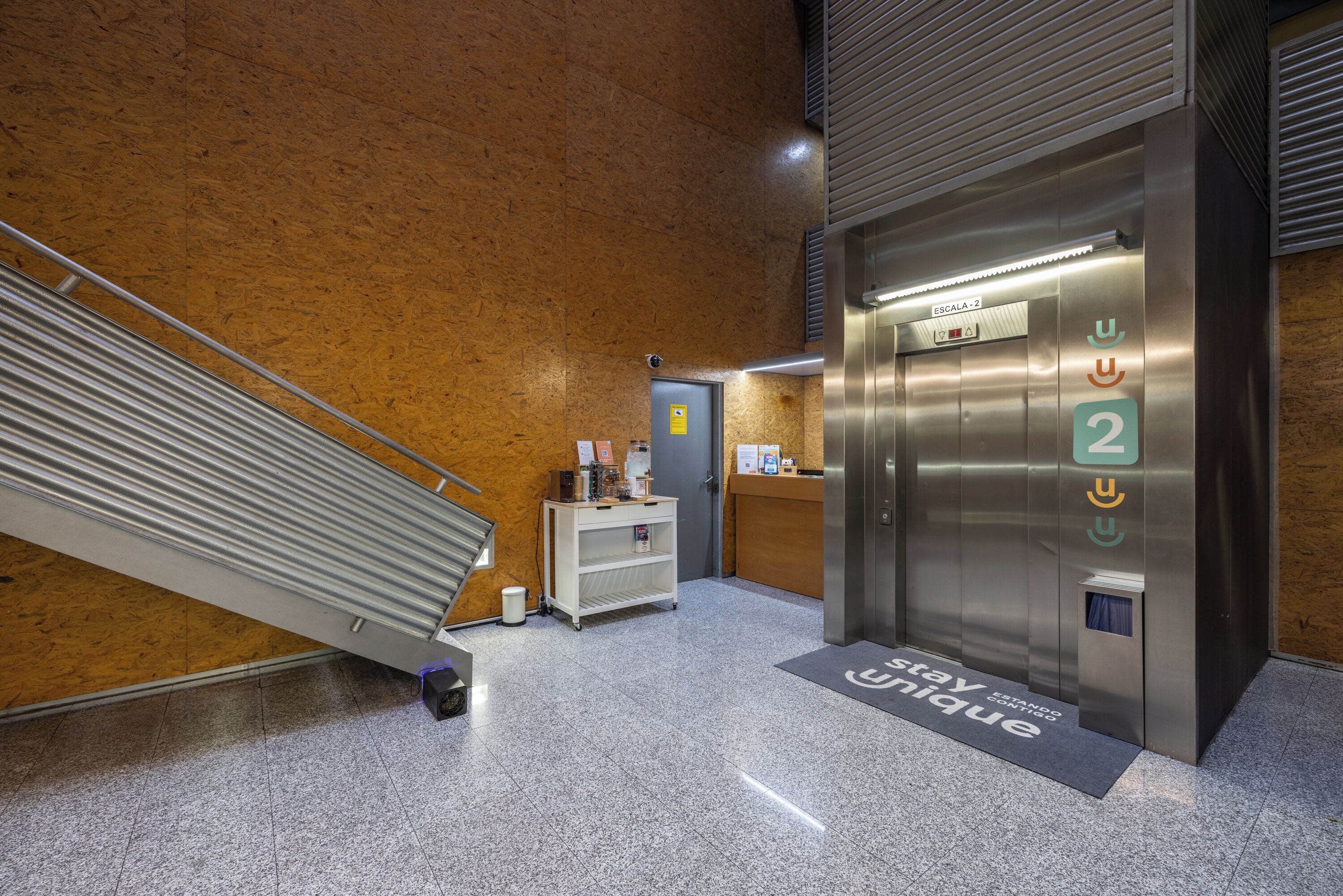 Een lift met een digitaal scherm, een receptiebalie en een trap.
