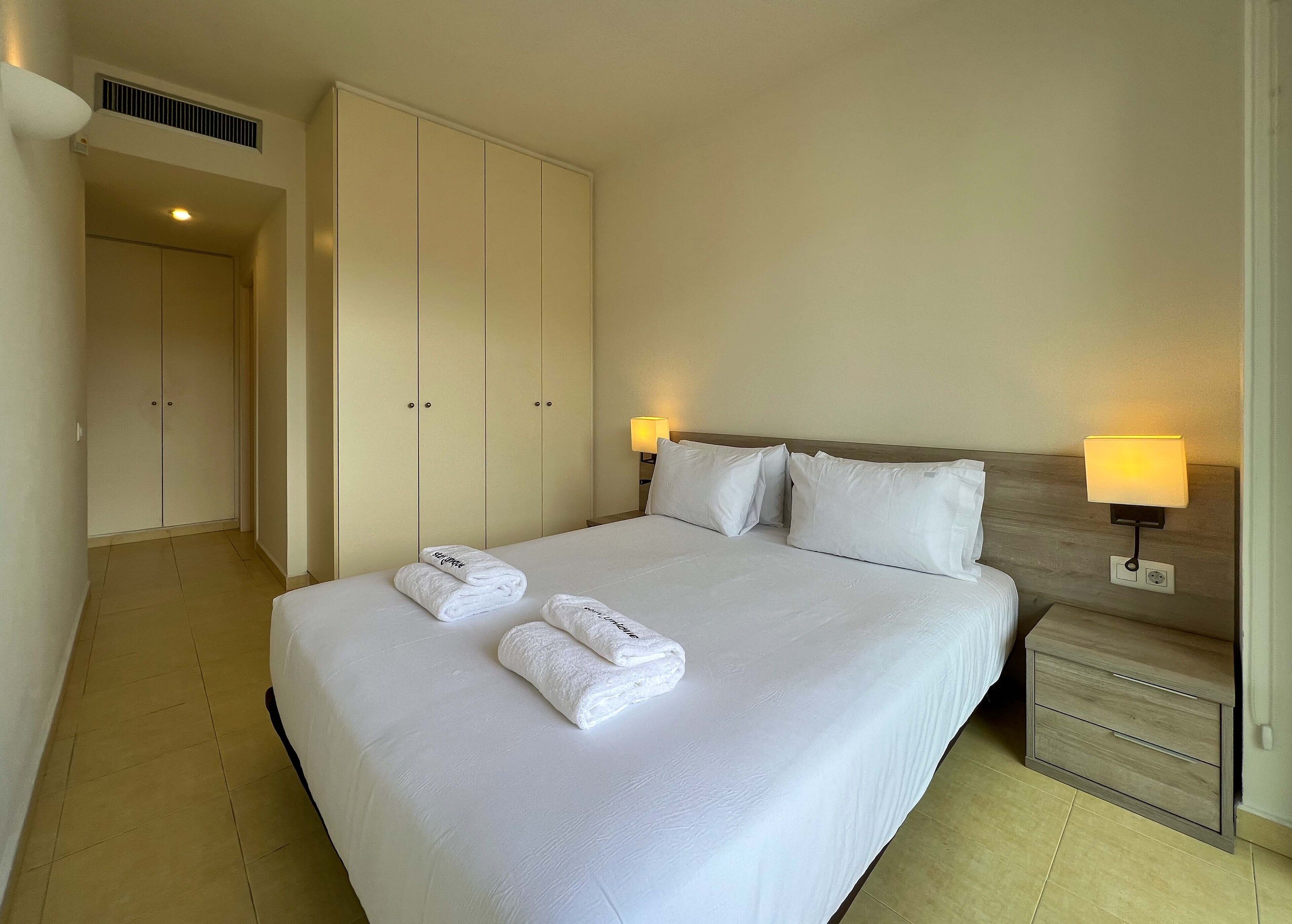 Ein Hotelzimmer mit einem großen Bett, zwei Nachttischlampen, einem Holznachttisch und einem Kleiderschrank.