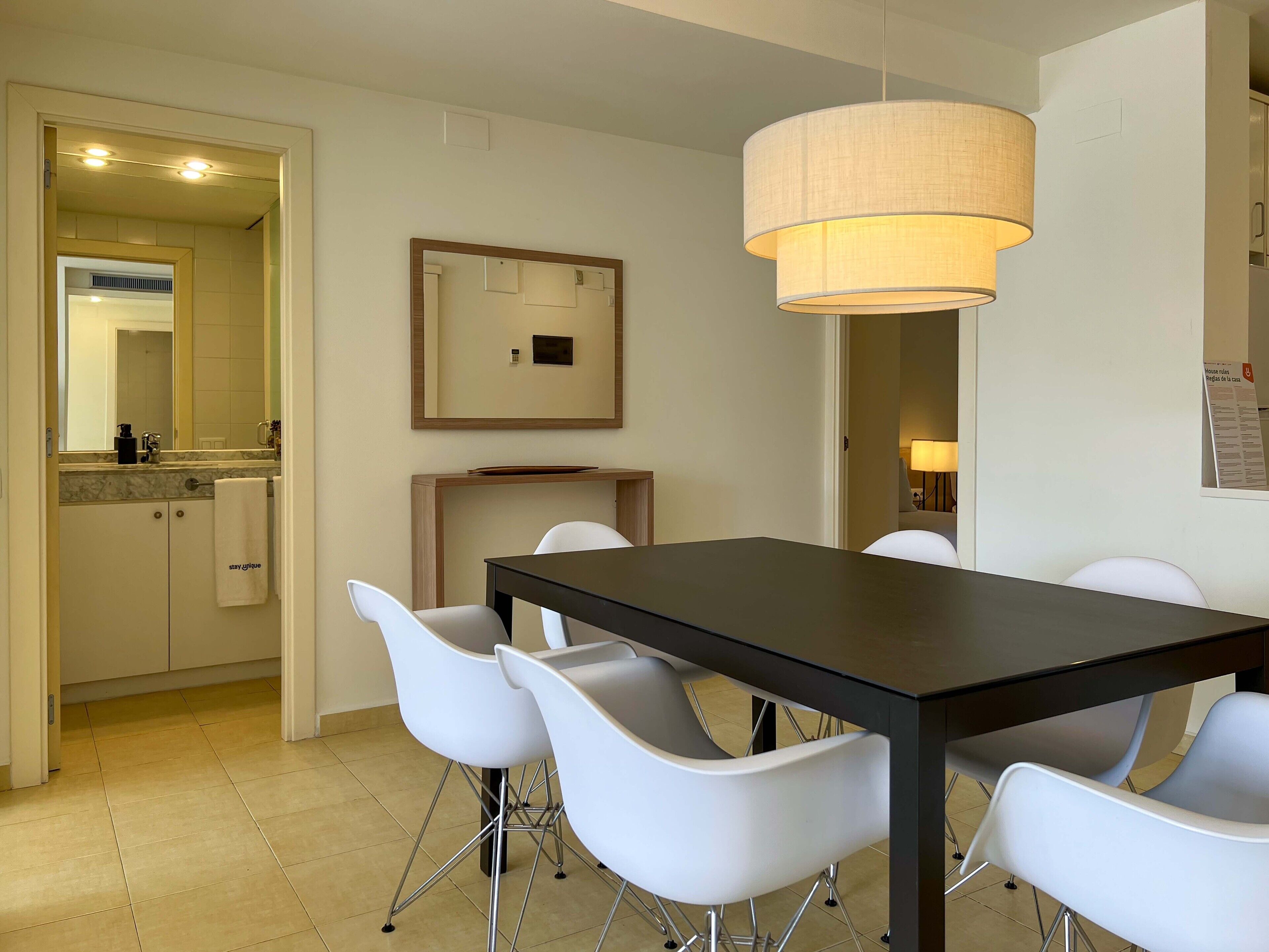 A modern dining area with a black table and white chairs, a pendant light, and a mirror on the wall.