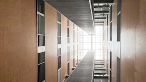 Een lange, smalle gang met een centrale trap, aan weerszijden bekleed met muren met verticale ventilatieroosters en een plafond met een lijnpatroon.