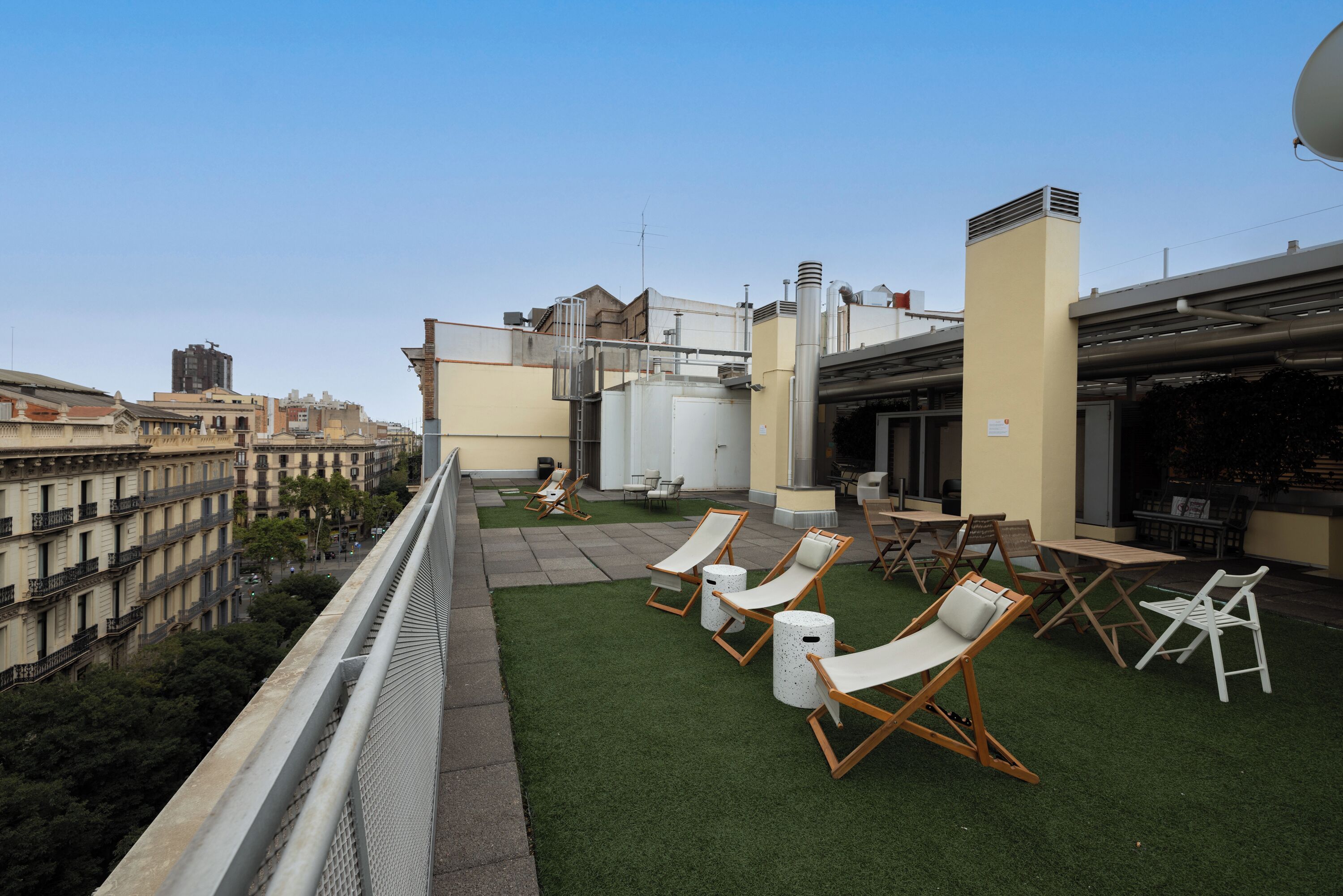 Une terrasse sur le toit, dotée d’un revêtement d’herbe artificielle, de chaises longues et offrant une vue sur le paysage urbain.
