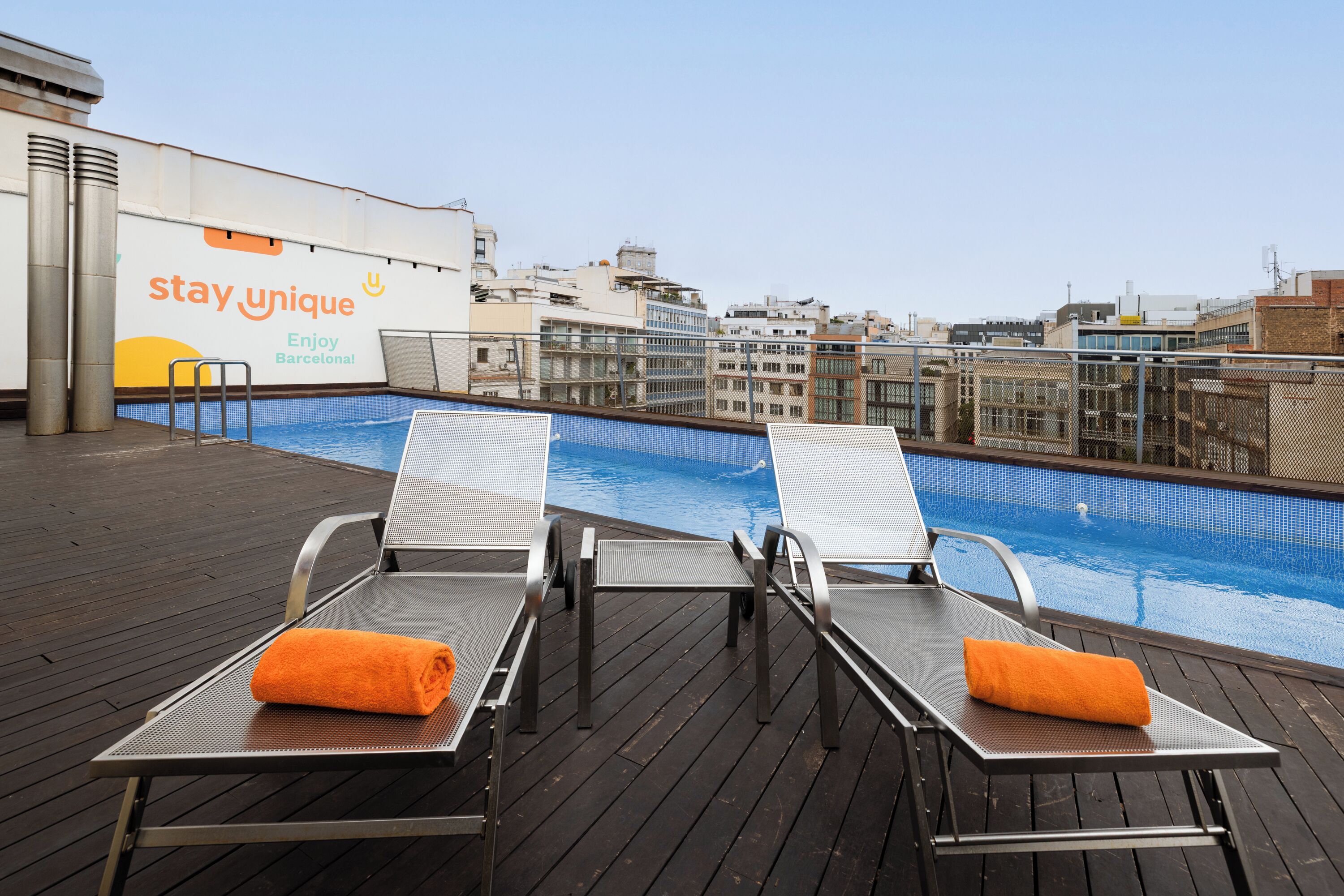 A rooftop pool area with lounge chairs and a 'stay unique' advertisement.