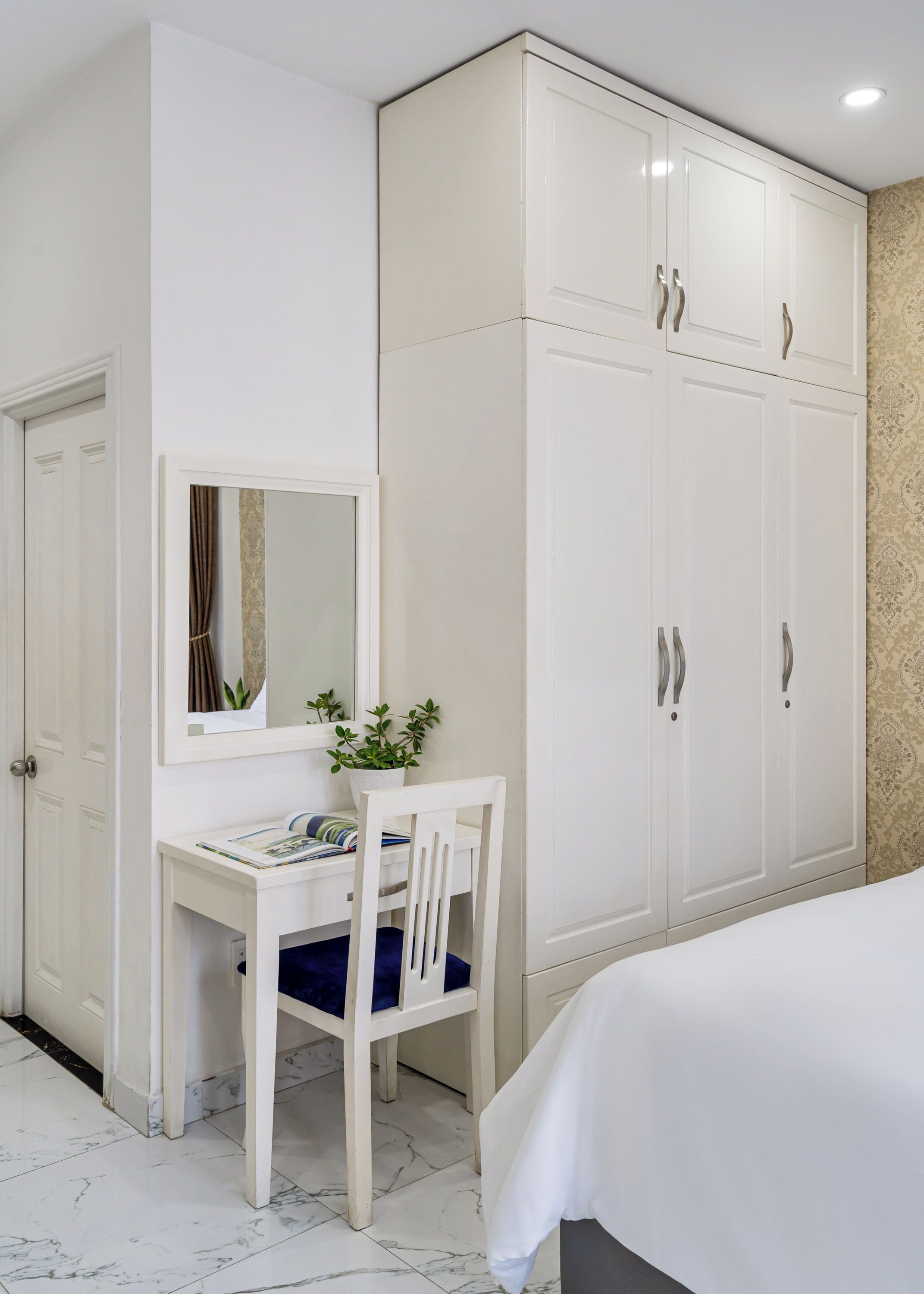 Un dormitorio con cama, un armario blanco, un escritorio con silla y un espejo.