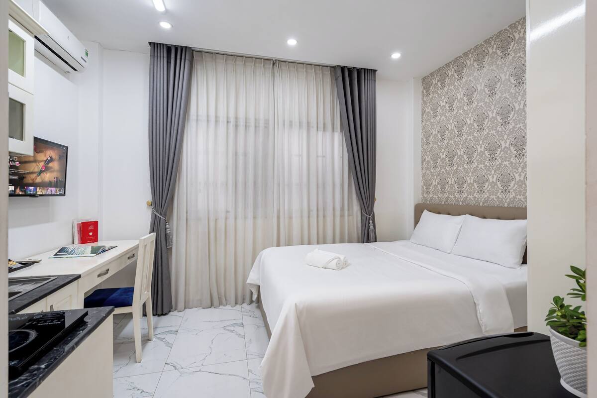 A hotel room with a bed, a desk with a chair, a television, and a potted plant.