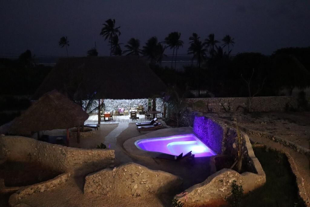 Ein Gebäude mit einem Strohdach, einem Pool und einer Lounge-Bereich, umgeben von Palmen.