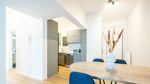 A modern kitchen with grey cabinets, a wooden dining table, and blue chairs. - Urban Comfort 2 Bdrm Next to Metro (Athens)