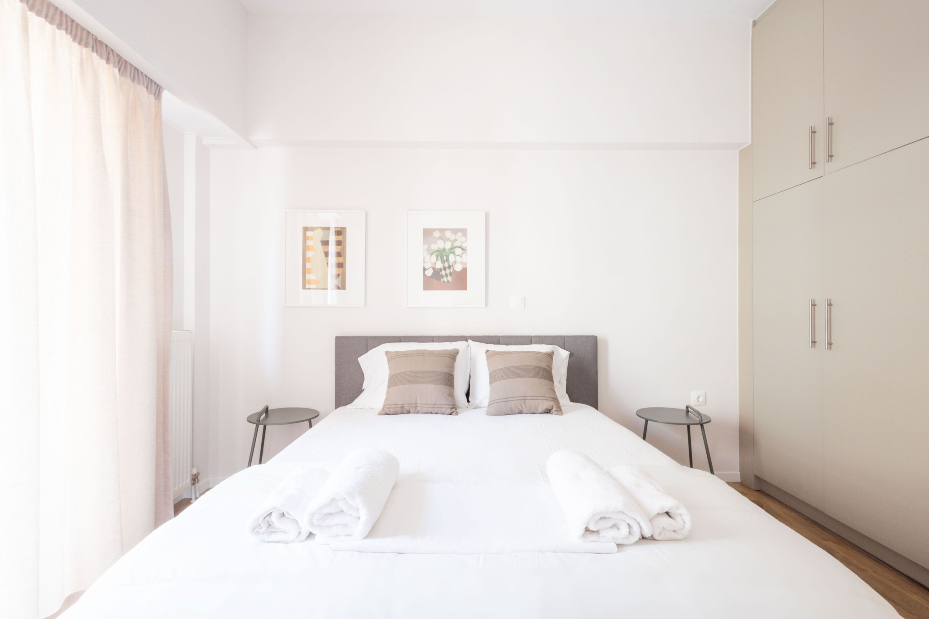 A neatly made bed with white linens and two pillows, a small bedside table, and a wall-mounted artwork.