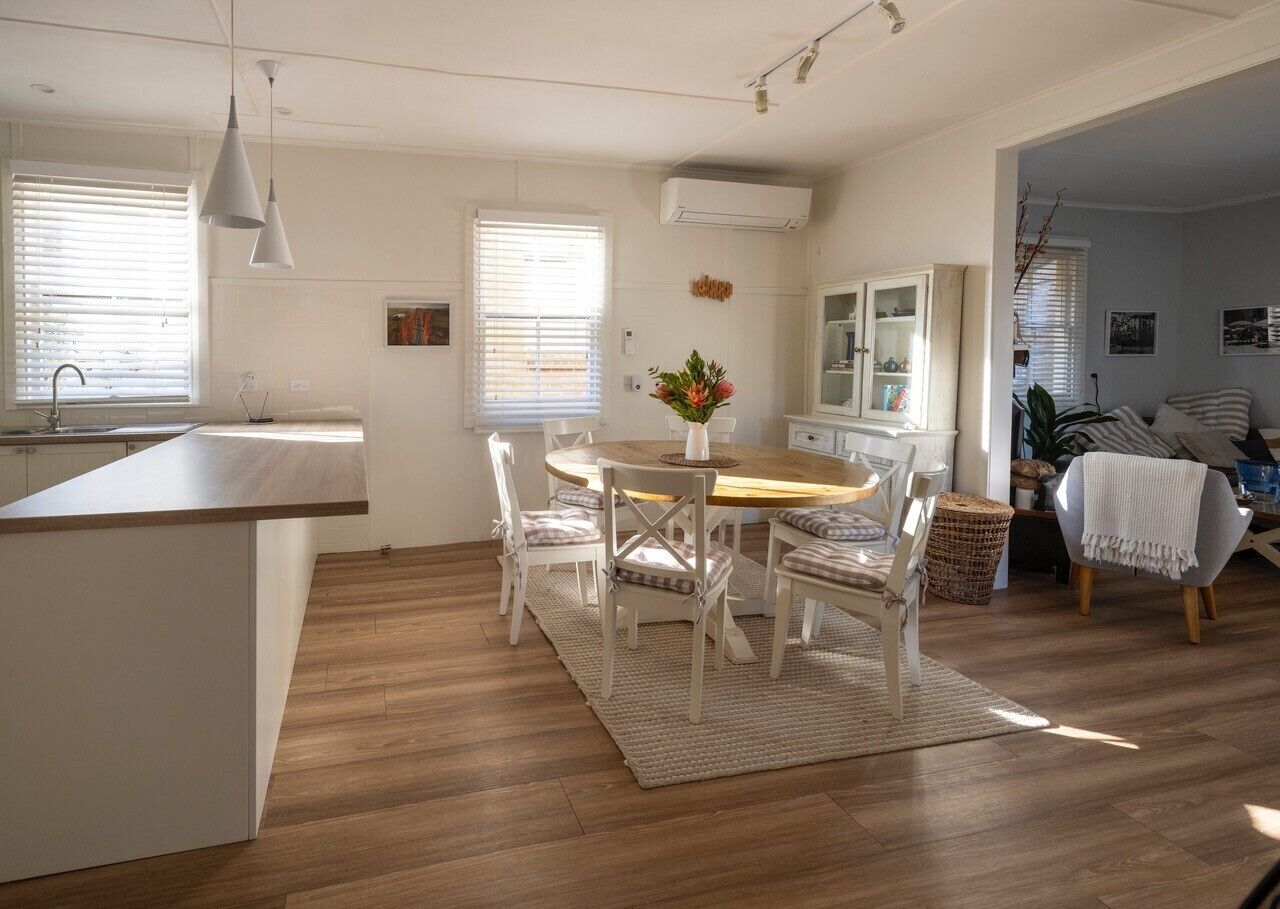 Une cuisine moderne avec une table à manger en bois, des chaises blanches et un îlot central.