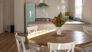 A kitchen with a round wooden table, white chairs, a teal refrigerator, a stove, and a window with blinds. - Nelly's Cottage Braidwood - cosy cottage in a picture perfect country setting (Braidwood)