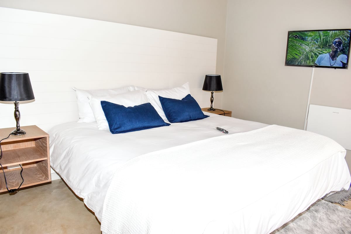 A hotel room with a large bed, two bedside tables with lamps, a flat-screen TV on the wall, and a small wooden nightstand.