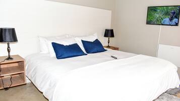 A hotel room with a large bed, two bedside tables with lamps, a flat-screen TV on the wall, and a small wooden nightstand.