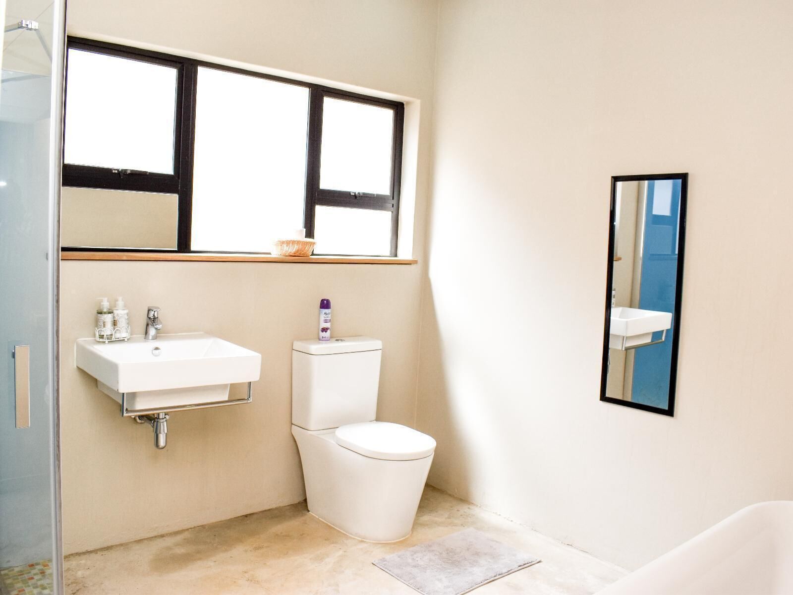 Un baño con lavamanos blanco, inodoro y ventana sobre el lavamanos.