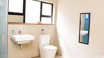 Un baño con lavamanos blanco, inodoro y ventana sobre el lavamanos.