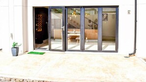 Un edificio moderno con entrada de vidrio, una escalera que sube a un piso superior y una planta en maceta afuera.