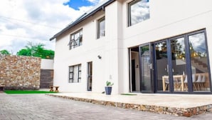 Una casa moderna de dos pisos con muro de piedra, ventanas amplias y un patio con mobiliario exterior.