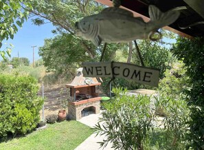 A 'WELCOME' sign above a barbecue area surrounded by greenery. - Sias Cozy House (Sithonia)