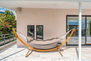 A hammock chair on a balcony with a view of a building and trees. - Alimos Luxury 3Bd w Outdoor Jacuzzi (Alimos)
